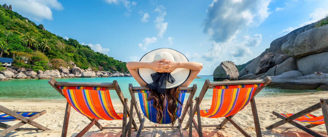 Woman with hat sitting on chairs beach in beautiful tropical bea