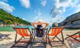 Woman with hat sitting on chairs beach in beautiful tropical bea